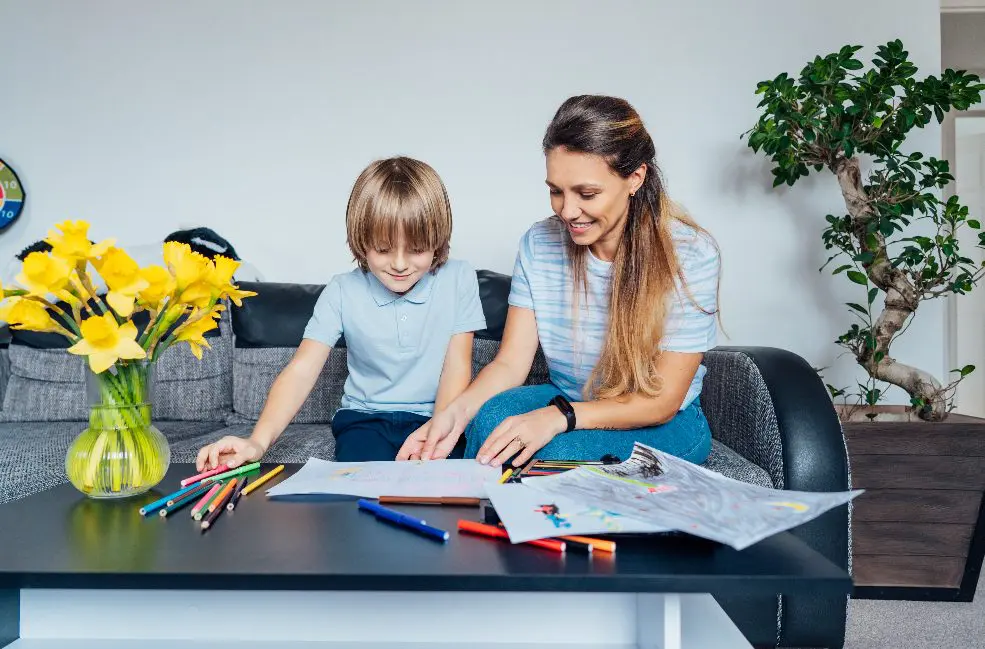 Mère et fils dessinent avec des crayons de couleur et des marqueurs dans le salon.